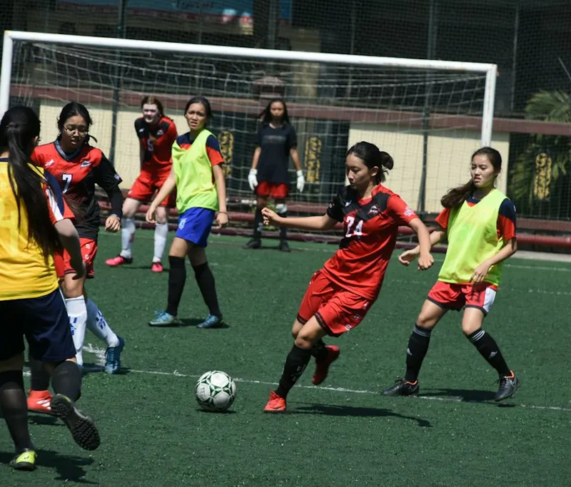 Stock photo of girls in red and yellow bibs playing football on a green pitch in front of a goal.